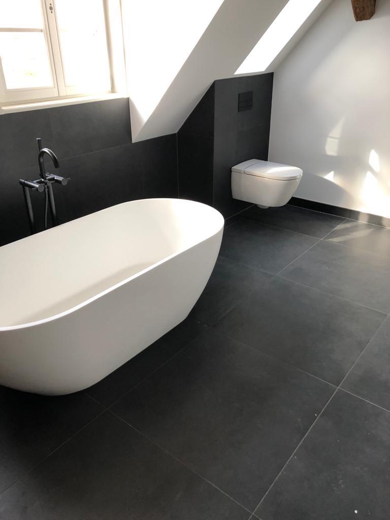 Bad mit schwarzen Wandfliesen und freistehender weißer Badewanne