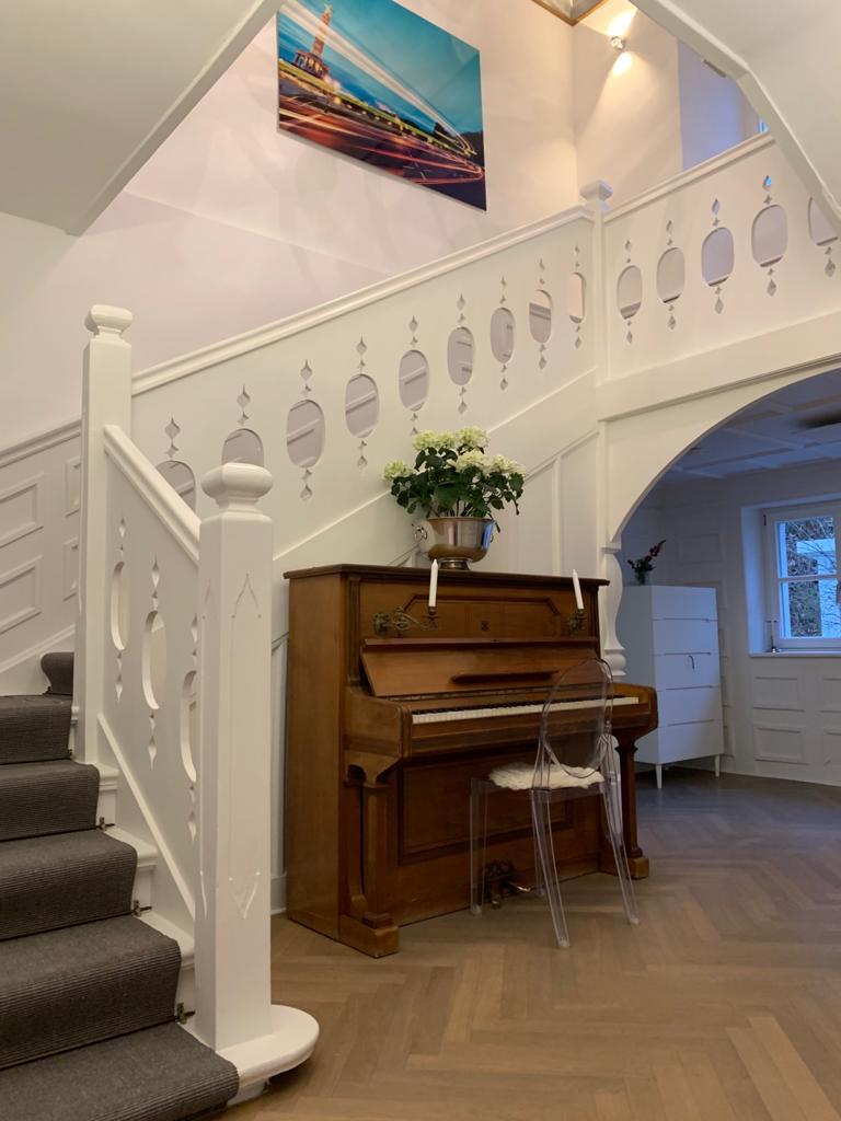 Heller Wohnflur mit weißer geschnitzter Treppe, Klavier und Fischgrät-Parkett